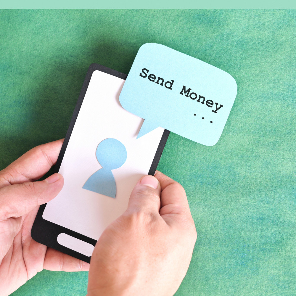 person holding mobile phone with a fake note with text "send money..."