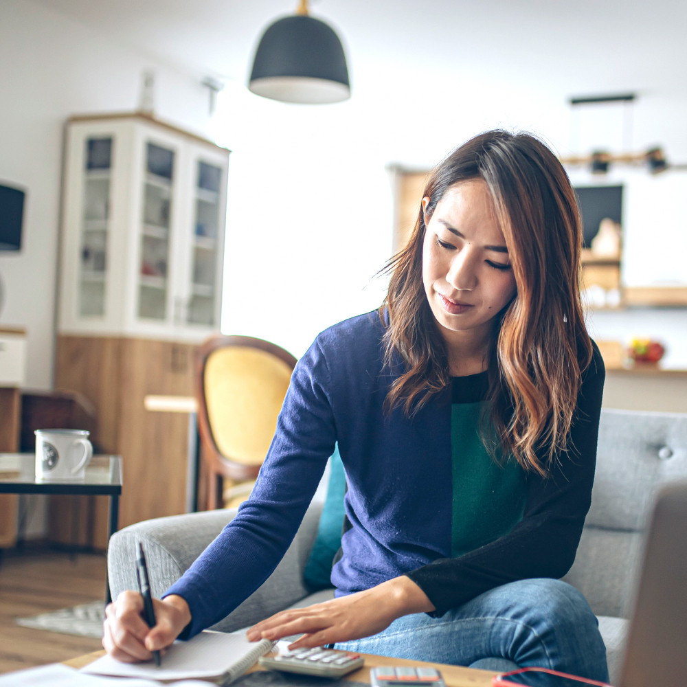 Woman writing in a notebook sitting in her living room