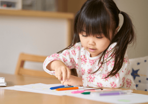 a little girl in pigtails coloring at the kitchen table