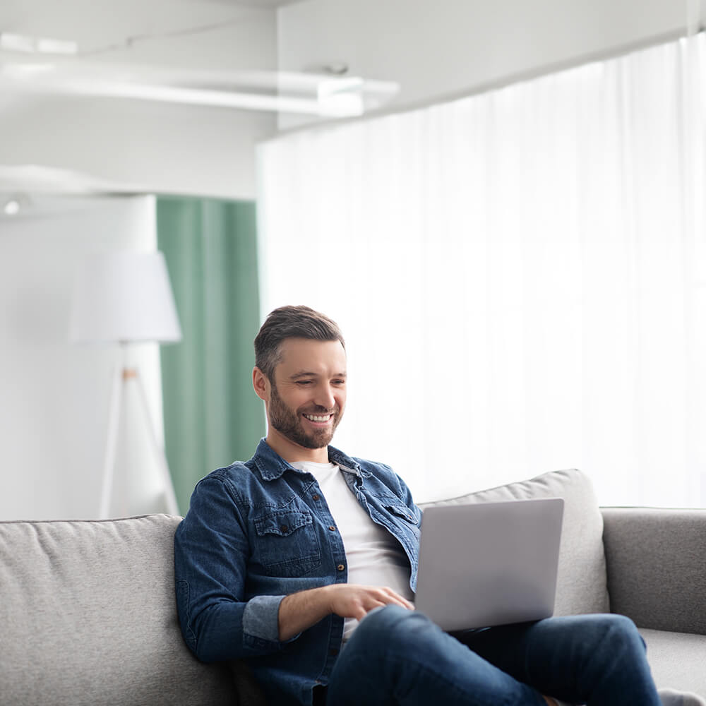 man sitting on his couch smiling at his credit score on his computer