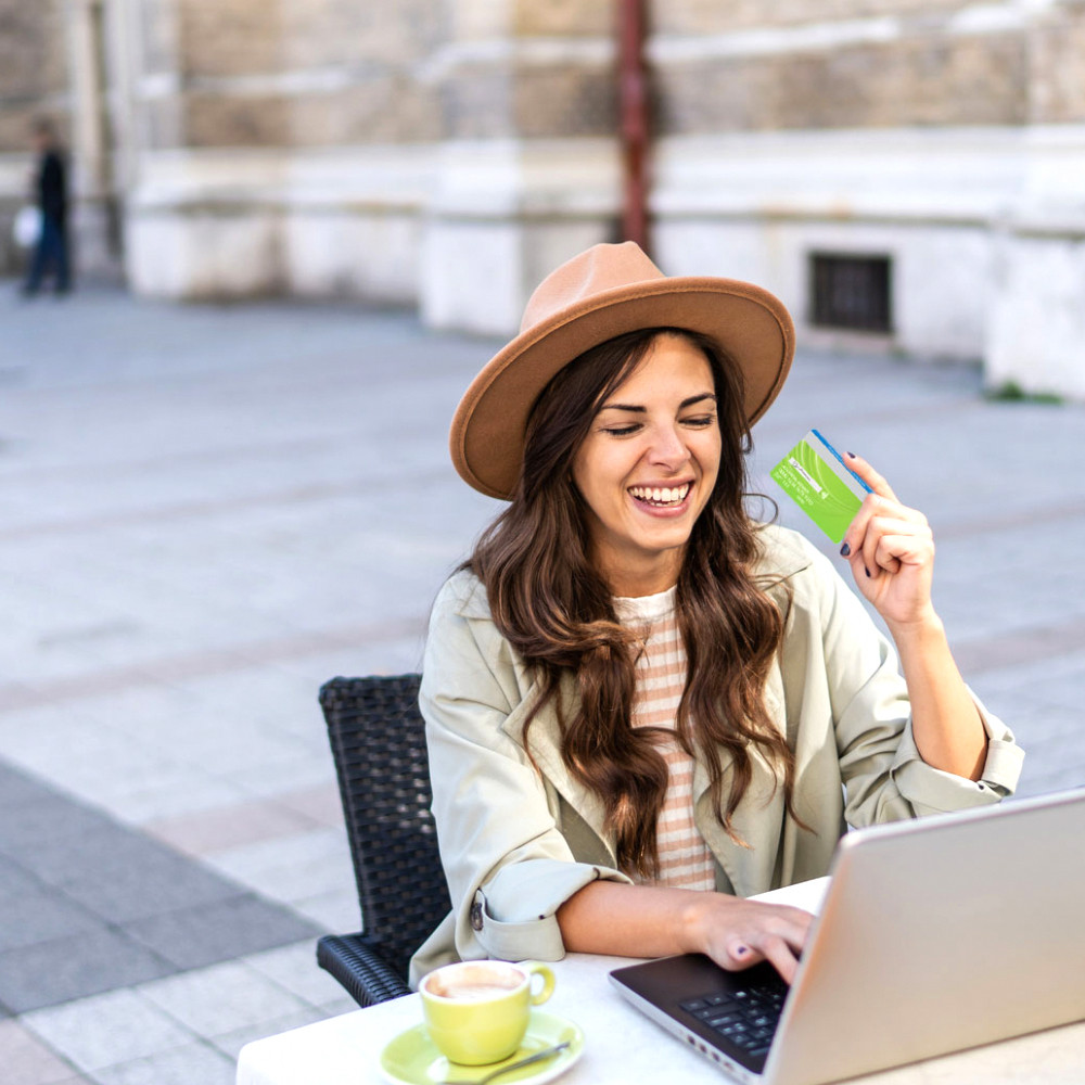 Smiling woman on laptop holding Ultimate Checking debit card