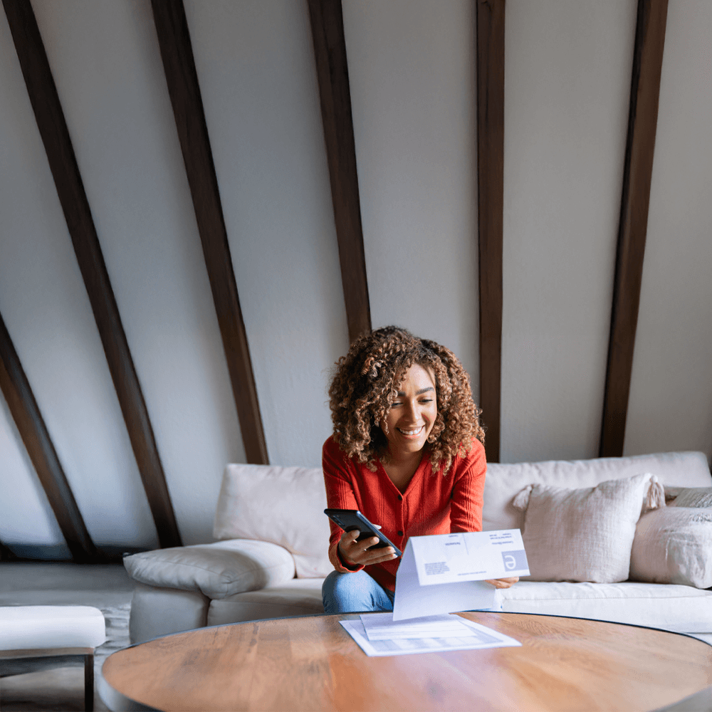 smiling woman holding her phone and looking at her bills