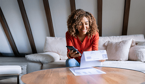 smiling woman holding her phone and looking at her bills