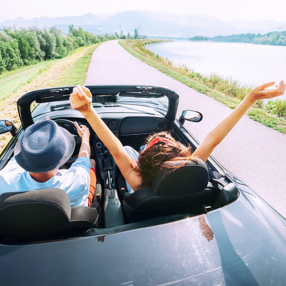two people driving in a convertable on the open road