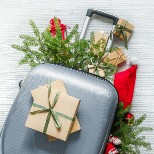 suitcase surrounded by christmas tree stems and gifts