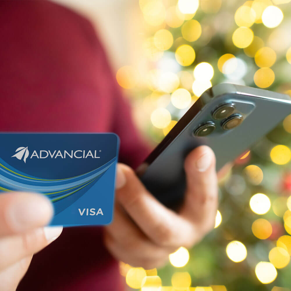 concerned woman by a christmas tree looking at her phone and holding her credit card