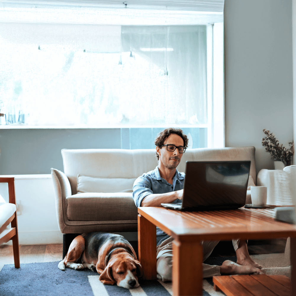 man on his laptop in the living room next to his dog