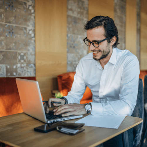 man working in a cafe smiling at his laptop